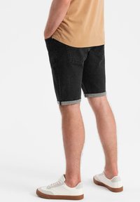 Bermudas de mezclilla negras con dobladillo enrollado, que presentan un diseño clásico de cinco bolsillos y una textura suave, lucidas con zapatillas blancas.
