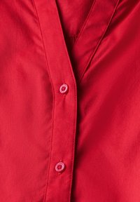 Rotes Hemd mit Knöpfen aus glattem Stoff, das über einen tiefen V-Ausschnitt verfügt, mit runden, passenden roten Knöpfen und sichtbaren Nahtdetails.