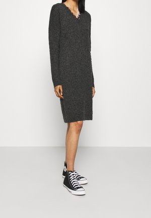 Femme portant une robe en maille gris foncé à manches longues avec un col en V orné de dentelle et des baskets montantes noires avec des lacets et semelles blanches.