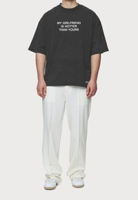 Black oversized t-shirt with white text "MY GIRLFRIEND IS HOTTER THAN YOURS," paired with white trousers and white sneakers.