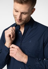 Granatowa koszula zapinana na guziki, wykonana z gładkiego materiału, z kieszenią z logo, slim fit oraz widocznymi detalami guzików na mankietach.