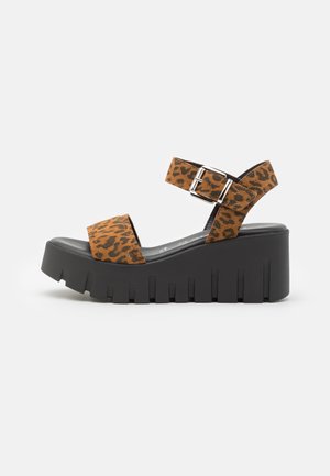 Platform sandals with leopard print fabric straps and a chunky black rubber sole featuring a ridged design and adjustable buckle.