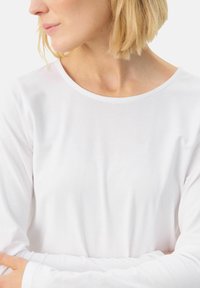 White long-sleeve top with a soft, smooth texture and a rounded neckline. Simple design with no visible patterns or accents.