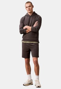 Sudadera de manga larga gris oscuro superpuesta sobre una camiseta amarilla clara, combinada con pantalones cortos a juego y zapatillas crema, con calcetines blancos.