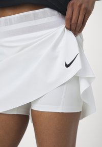 Falda atlética blanca con un diseño en capas, que cuenta con una cinturilla de malla transpirable y un pequeño logo negro de Nike en el costado.