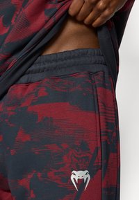 Αθλητικό σορτς σε σκούρο ναυτικό χρώμα με μπορντό αφηρημένα σχέδια, ελαστική μέση και ασημένια διακοσμητική λογότυπο. Κατασκευασμένο από απαλό, διαπνέον υλικό.