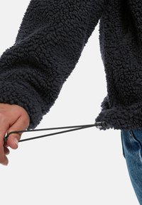 Herenfleece pullover in houtskool met een gestructureerd oppervlak. Verstelbaar trekkoord aan de zoom vastgehouden door een hand. Casual ontwerp, lange mouwen en een relaxte pasvorm.
