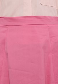 Gros plan d’une personne portant une jupe rose avec une large ceinture et une chemise rose clair rentrée à l’intérieur.