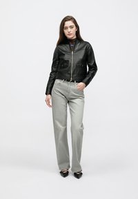 Černá kožená krátká bunda se zipem vpředu, dvě přední kapsy, v kombinaci se šedými džínami s rovnými nohavicemi a černými botami s špičatou špičkou.