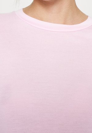 Nahaufnahme einer Person, die ein hellrosa T-Shirt mit Rundhalsausschnitt trägt, das den Hals- und oberen Brustbereich zeigt.