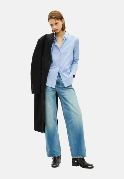 Niebieska koszula z guzikami, czarny długi płaszcz, szerokie jasnoniebieskie dżinsy i czarne botki za kostkę z srebrnymi akcentami. Gładki materiał, casualowy krój.