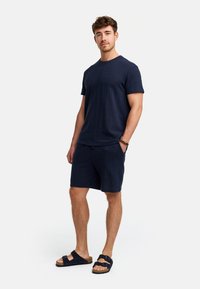 Marineblaue Kurzarm-T-Shirt mit einem strukturierten Muster, kombiniert mit passenden Shorts und schwarzen Sandalen mit einem Schnallen-Detail.
