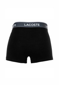 Boxer in cotone nero con elastico grigio che presenta il logo "LACOSTE" in bianco. Texture liscia, design aderente con taglio corto.