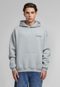 Hanorac gri deschis, realizat dintr-un amestec de bumbac, cu o buzunare tip kangaroo, manșete ribbate și un logo brodat "ANOTHER COTTON" pe piept.
