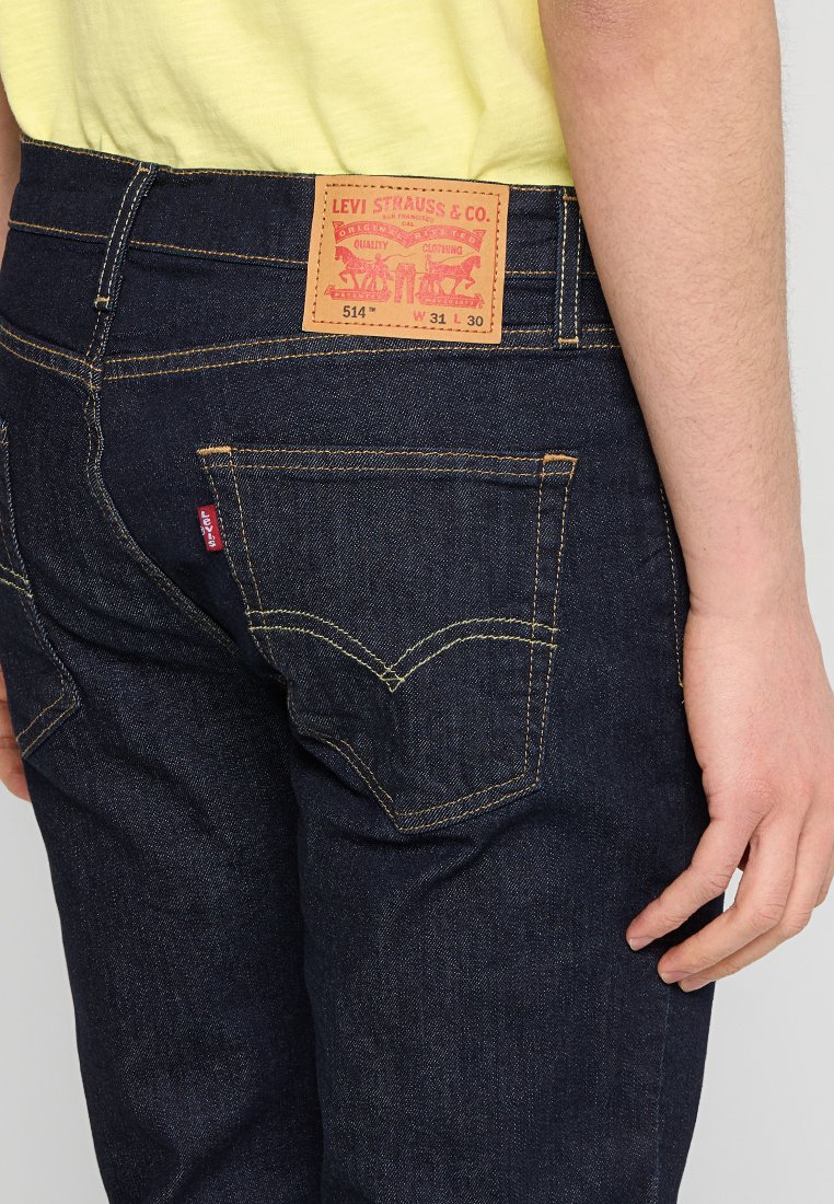 Ciemnoniebieskie dżinsy Levi's z brązową skórzaną naszkicowaną łatą z czerwonym nadrukowanym logo z tyłu. Kontrastowe przeszycia i klasyczny design kieszeni.