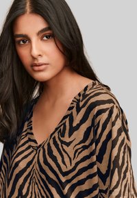Top bej cu decolteu în V, decorat cu un model de dungi zebra negre, realizat dintr-un material moale, cu o croială lejeră și mâneci scurte.