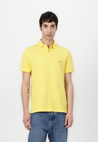 Cămașă polo galbenă din bumbac, cu guler, mâneci scurte și un mic logo pe pieptul stâng. Purtați-o cu blugi din denim albaștri.