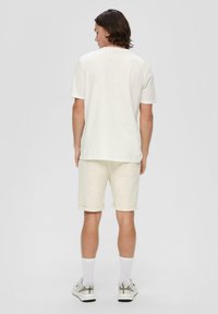 Helle beige Baumwoll-T-Shirt mit kurzen Ärmeln, kombiniert mit passenden beigen Shorts. Die Sneakers haben graue Akzente und weiße Socken.