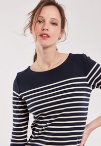 Haut à manches longues bleu marine avec des rayures horizontales blanches, col rond et texture de tissu douce, conçu pour un ajustement décontracté.