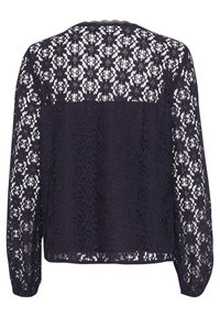 Blouse en dentelle bleu marine à manches longues, présentant des motifs floraux complexes et un panneau arrière uni. L'encolure festonnée ajoute une touche de détail.