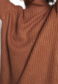 Kuscheliger Strickrollkragenpullover in sattem Rostton, mit geripptem Muster und übergroßen Ärmeln für einen lässigen Sitz.
