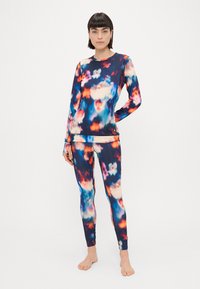 Top atlético de mangas longas e leggings feitos de tecido elástico com um padrão colorido de tie-dye em tons de azul, rosa e laranja.