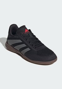 Zwarte sportieve schoen met een bovenkant van netstof, grijze strepen, gevoerde kraag en rood logo. Beschikt over een rubberen zool die is ontworpen voor grip en duurzaamheid.