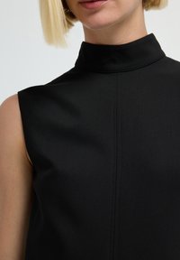 Schwarzes ärmelloses Oberteil mit hohem Kragen, glatter Textur und subtilen Nähten. Minimalistisches Design, das modernen Stil betont.