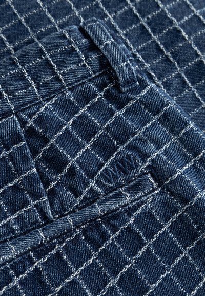 Dark blue denim fabric with a white grid pattern, showing a close-up of a belt loop and pocket stitching.