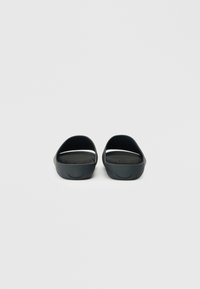 Μαύρες καουτσούκ σανδάλες με ανοιχτή πλάτη, καμπυλωτό σχέδιο, υφασμάτινη επιφάνεια και διακριτές οπές αερισμού. Λείος φινίρισμα και μινιμαλιστικό στυλ.