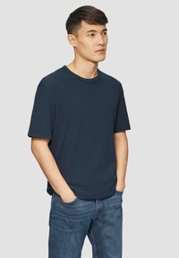 Granatowa koszulka z krótkim rękawem wykonana z teksturowanej tkaniny, z okrągłym dekoltem i luźnym krojem, zestawiona z jasnoniebieskimi dżinsami.