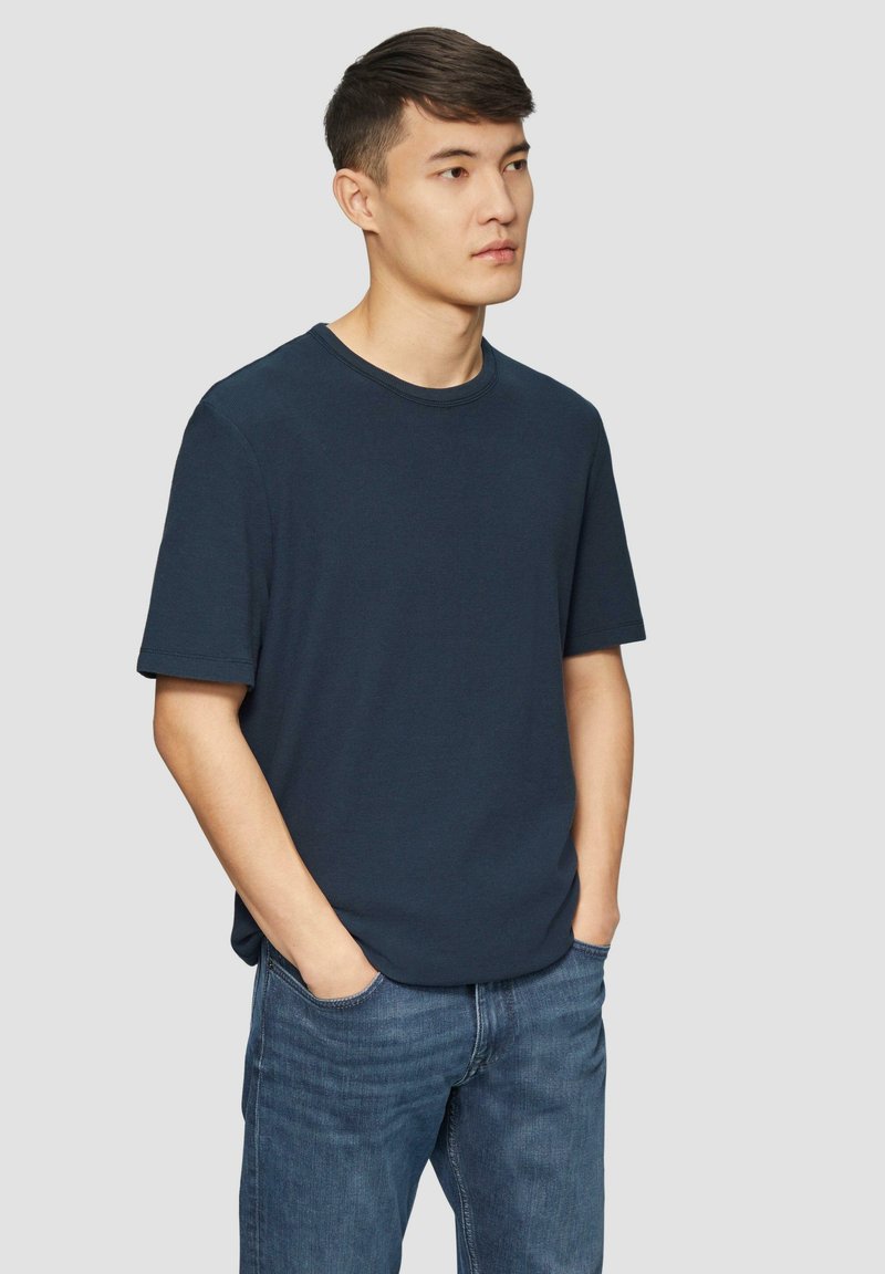 Granatowa koszulka z krótkim rękawem wykonana z teksturowanej tkaniny, z okrągłym dekoltem i luźnym krojem, zestawiona z jasnoniebieskimi dżinsami.