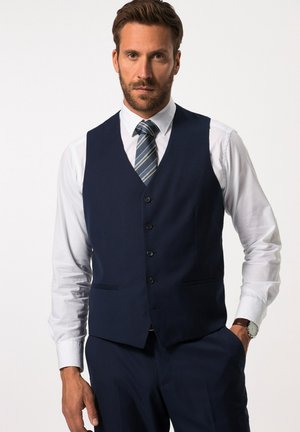 Gilet bleu marine en tissu texturé, avec un col en V, six boutons et deux poches avant. Associé à une chemise blanche et une cravate rayée.