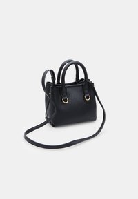Borsa a tracolla in pelle nera con due manici e una lunga tracolla regolabile, con anelli in metallo dorato su uno sfondo bianco semplice.