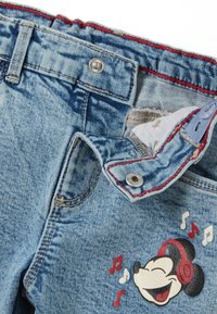Pantalones cortos de mezclilla con lavado azul claro, costuras rojas y un gráfico de Mickey Mouse usando auriculares con notas musicales.