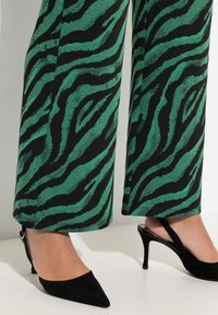 Gröna och svarta zebramönstrade vidbyxor med en texturerad yta, parat med spetsiga svarta slingback-klackar med en tunn stilettklack.