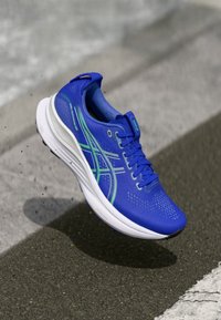 Blaue Laufschuhe mit Obermaterial aus Mesh, grünen Akzentlinien und gepolsterter weißer Sohle. Verfügt über ein Schnürdesign und eine strukturierte Oberfläche für Grip.