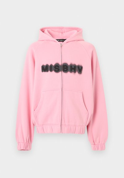 Sweat à capuche zippé rose avec poignets et ourlet élastiques, poches avant, et texte noir "MISBHV" en style flou sur la poitrine.