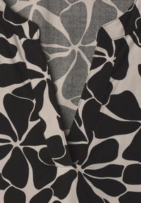 Vêtement à col avec un grand motif floral noir et beige et un décolleté en V laissant apparaître un tissu à motif assorti à l'intérieur.