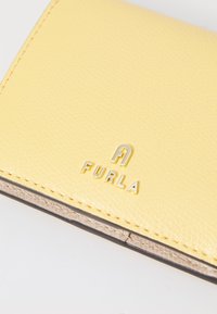 Yellow textured leather wallet with gold embossed "FURLA" logo. Features a smooth tan interior and visible stitching along edges.