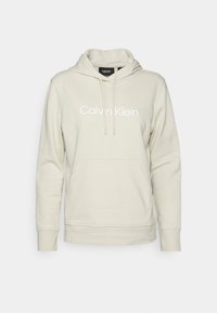 Sweat à capuche beige clair avec une poche avant, arborant un logo blanc "Calvin Klein". Confectionné en tissu doux avec des poignets et un ourlet côtelés.