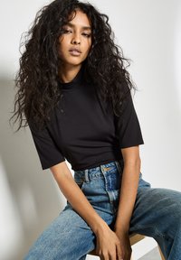 Top nero a maniche corte con collo alto abbinato a jeans di denim azzurri a vita alta caratterizzati da una texture sbiadita e una vestibilità morbida.