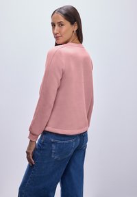 Felpa di pile rosa con scollo rotondo, polsini e orlo a coste; abbinata a jeans denim larghi blu scuro. Design minimalista, texture liscia.