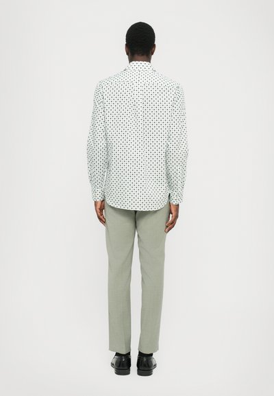 White shirt featuring a black circular pattern, paired with light grey trousers and black shoes, viewed from the back.