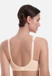 Beiger BH mit breitem Rücken, glatter Textur, verstellbaren Trägern und einem tiefen Ausschnitt. Mit Hakenverschluss und dezenten floralen Akzenten.