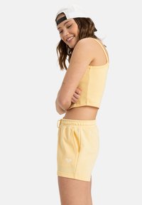 Geel cropped tanktop en bijpassende shorts, gemaakt van zachte stof. De shorts hebben een elastische tailleband en zijvakken. Witte logo-detail.