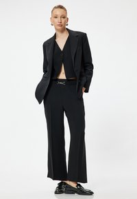 Svart skräddarsydd kostym med dubbelknäppt kavaj, kort topp och vida byxor. Utrustad med ett bälte med silverspänne och glänsande skor.