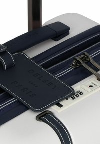 Valigia rigida con corpo bianco, dettagli in blu navy e maniglia texturizzata. Dotata di etichetta identificativa, lucchetto a combinazione e scomparto con zip.