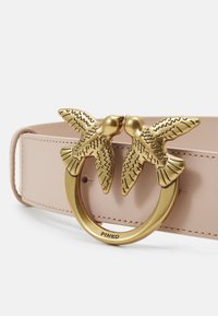 Rozā ādas jostas, kurai ir zeltainas metāla sprādzes forma, kas līdzinās diviem skūpstīgiem putniem. Gluda tekstūra ar izšūtiem segmentiem gar malām.