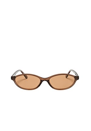 Lunettes de soleil ovales marron avec des montures étroites et des verres marron légèrement teintés, présentées sur un fond blanc uni.